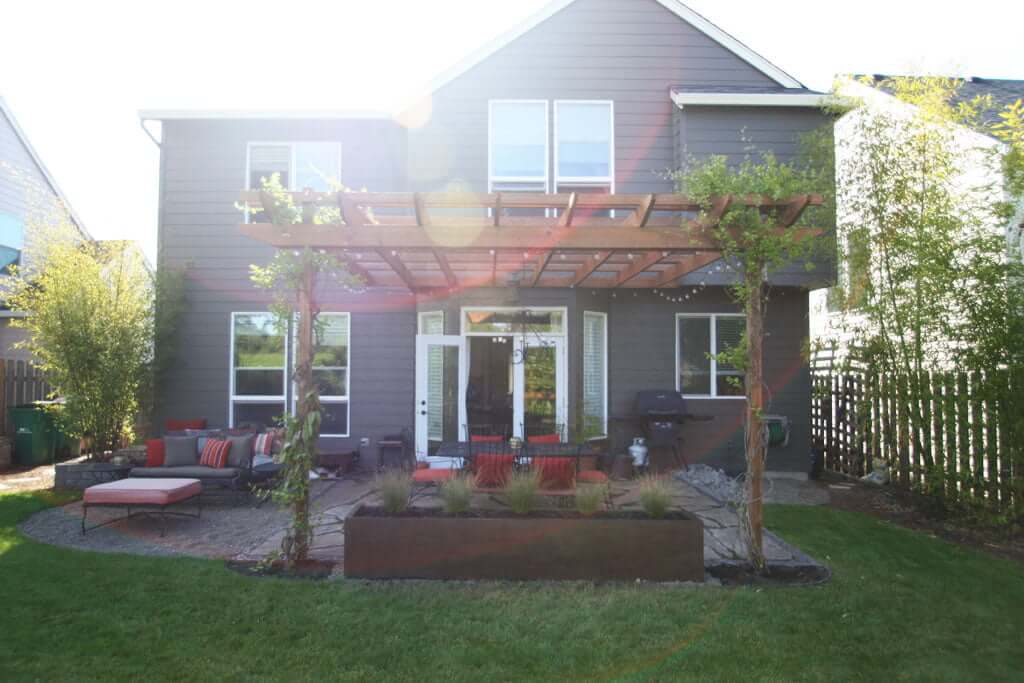 Back of house view with arbor, concrete planter, dining set, gravel firepit and bamboo