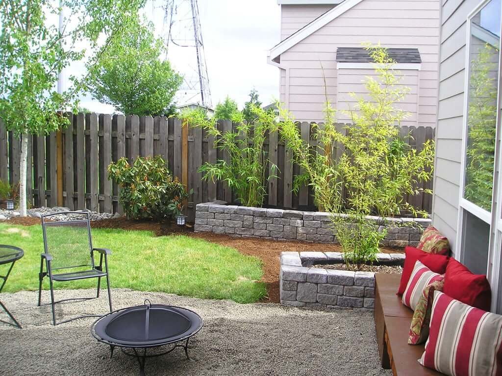 right side view of backyard with bamboo planters, large tree and gravel firepit in foreground