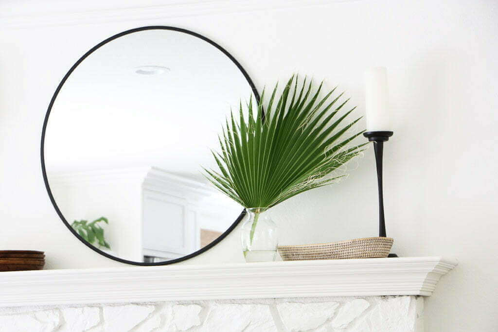fan palm in vase on top of mantle, with round mirror on wall