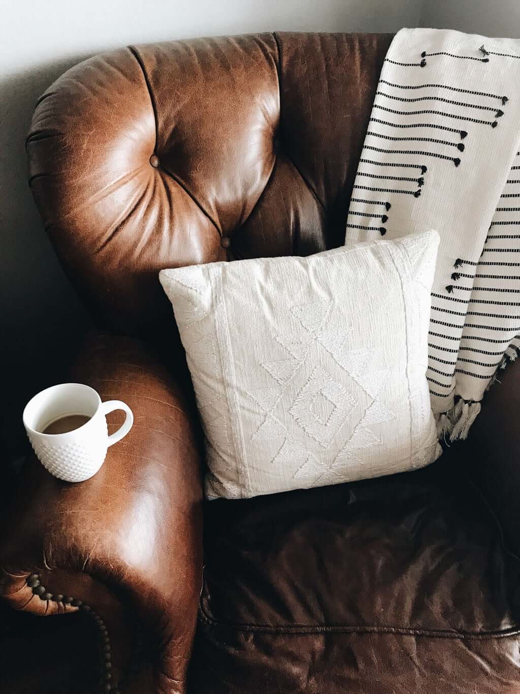leather chair with blanket, pillow, and coffee in mug