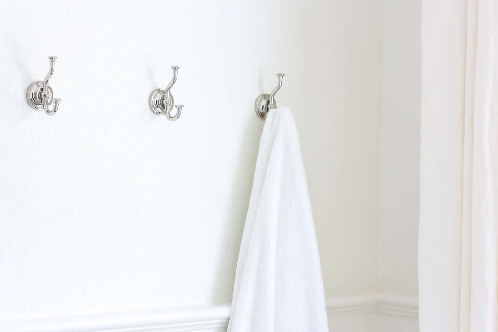 three polished nickel hooks on wall, with white towel hanging