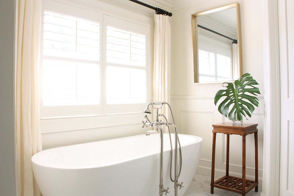 freestanding tub in bathroom with cream curtains behind