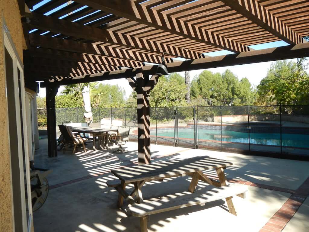 view under pergola to outdoor dining seating with pool in background