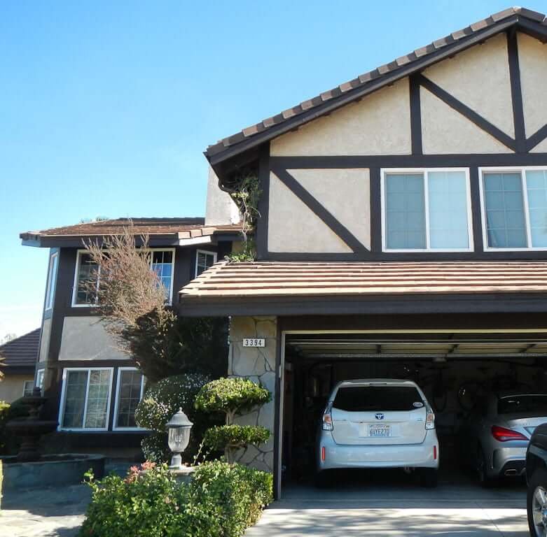 front of tudor-style house with overgrown bushes and open garage