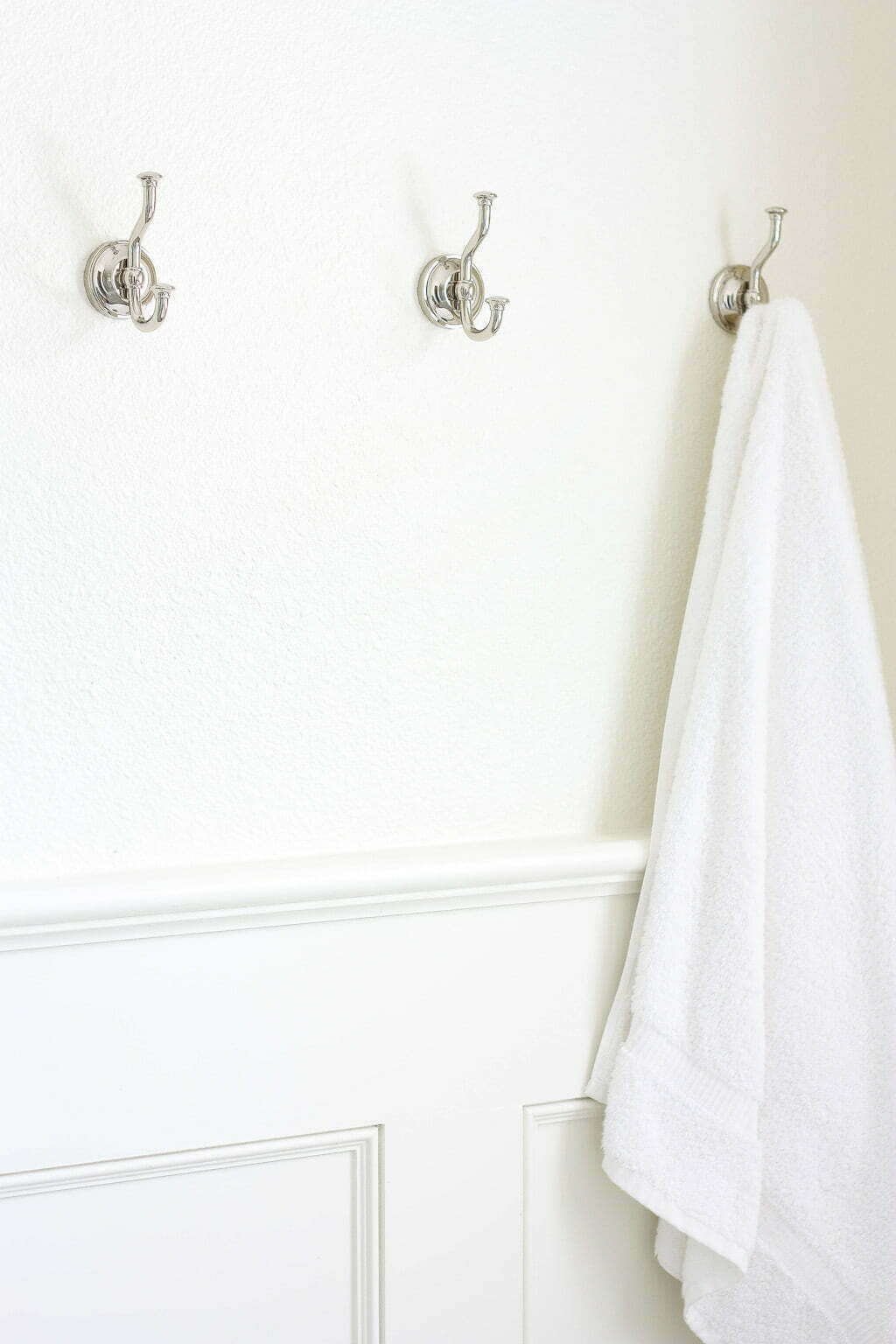 polished nickel hooks n bathroom with towel hanging, wainscoting on wall