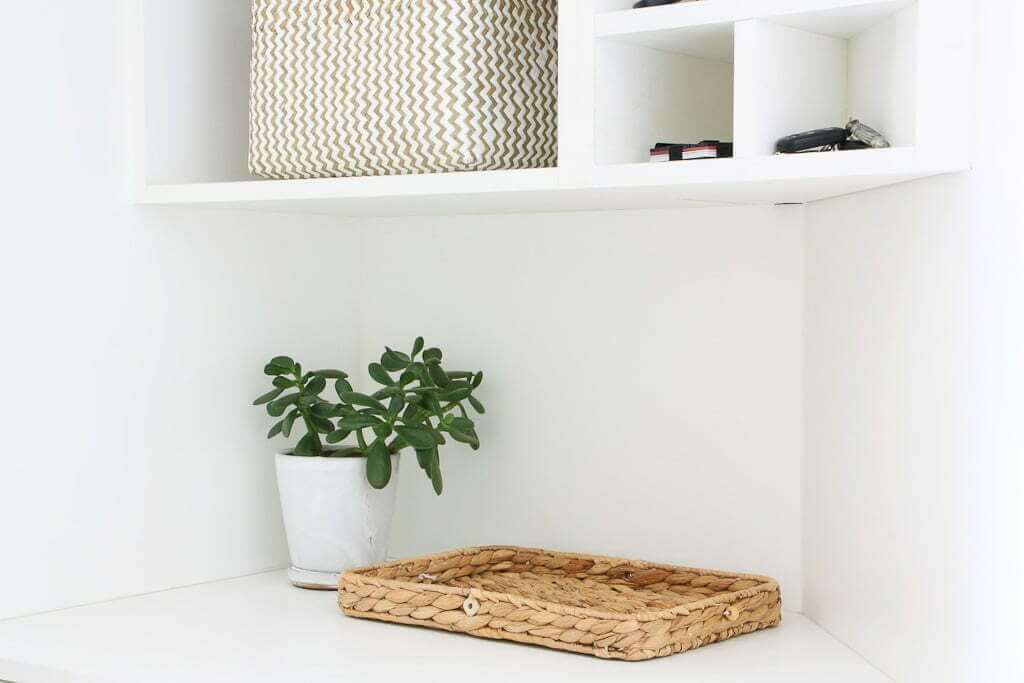 mudroom storage shelf with basket, plant, shelves above and small cubbies with keys and wallet