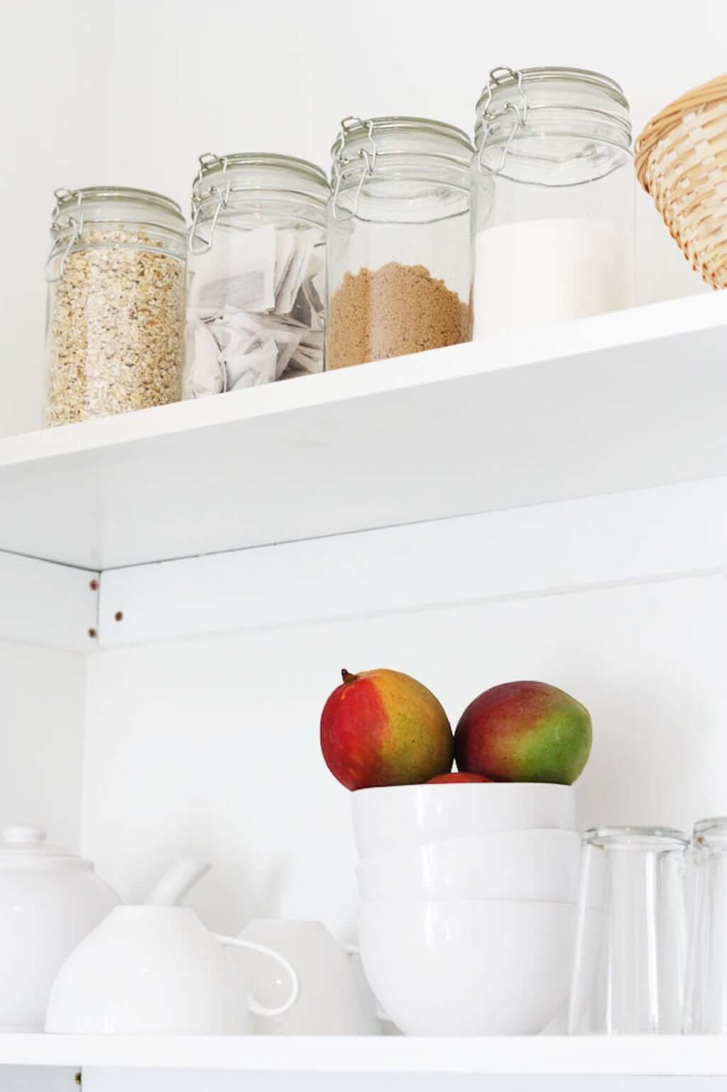 Containers on shelf with sugar and tea and mangoes in bowl