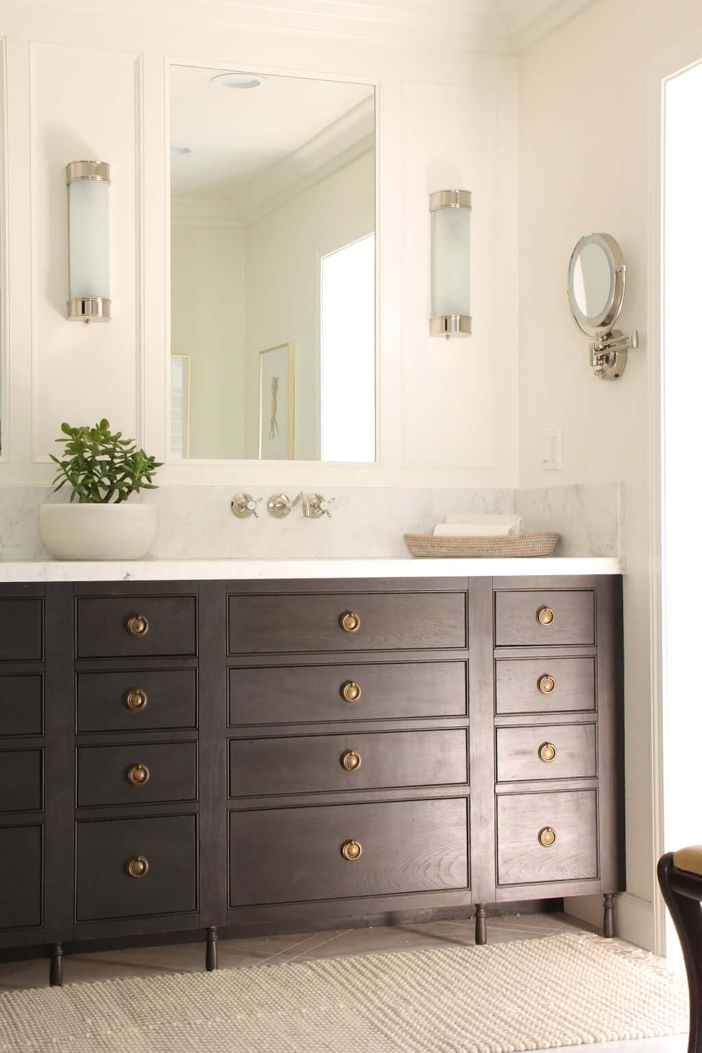 one side of master bathroom double vanity, wood with marble counter and brass ring pulls, wall-mounted faucet in polished nickel and wall sconces