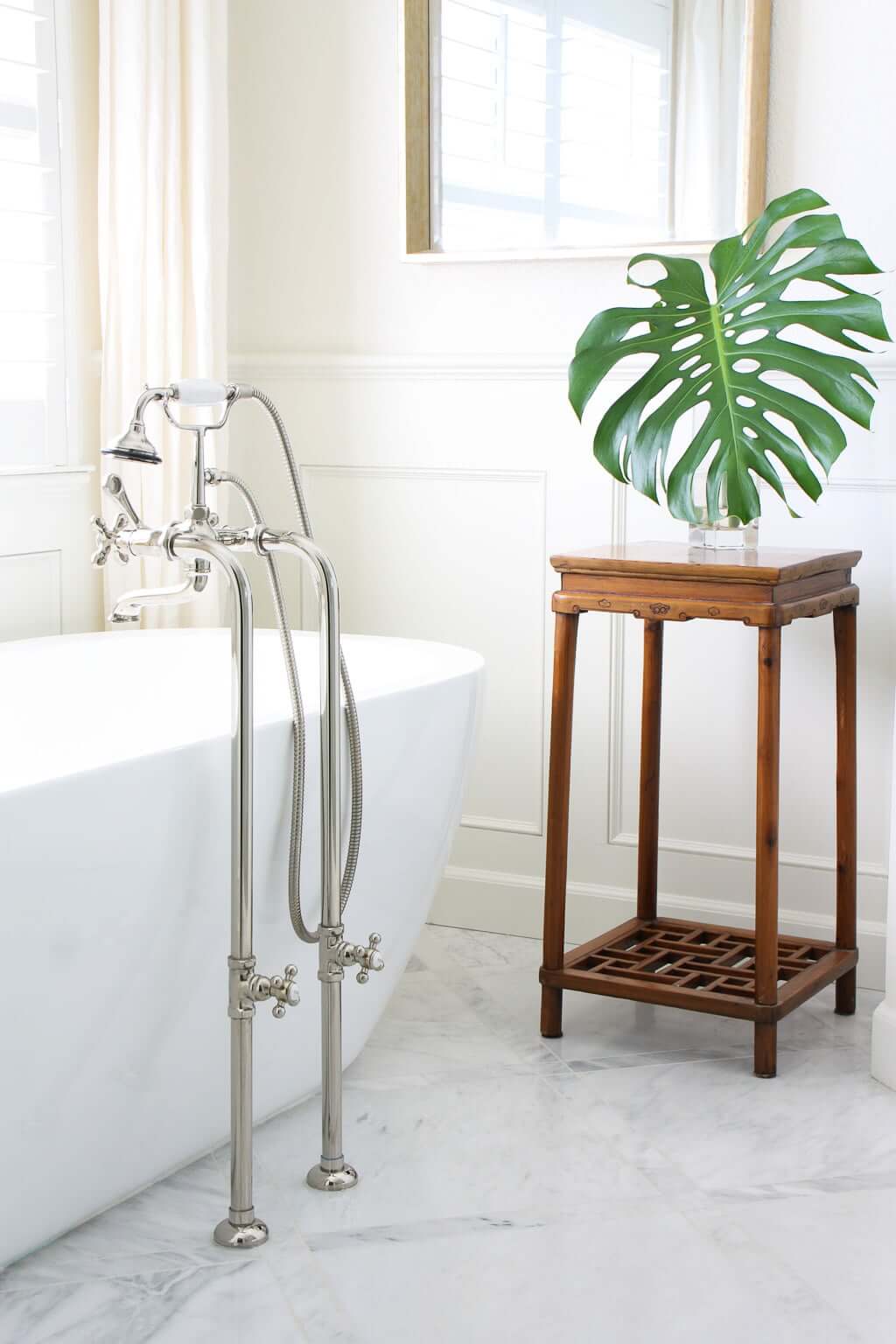 freestanding tub with marble floors and antique plant stand
