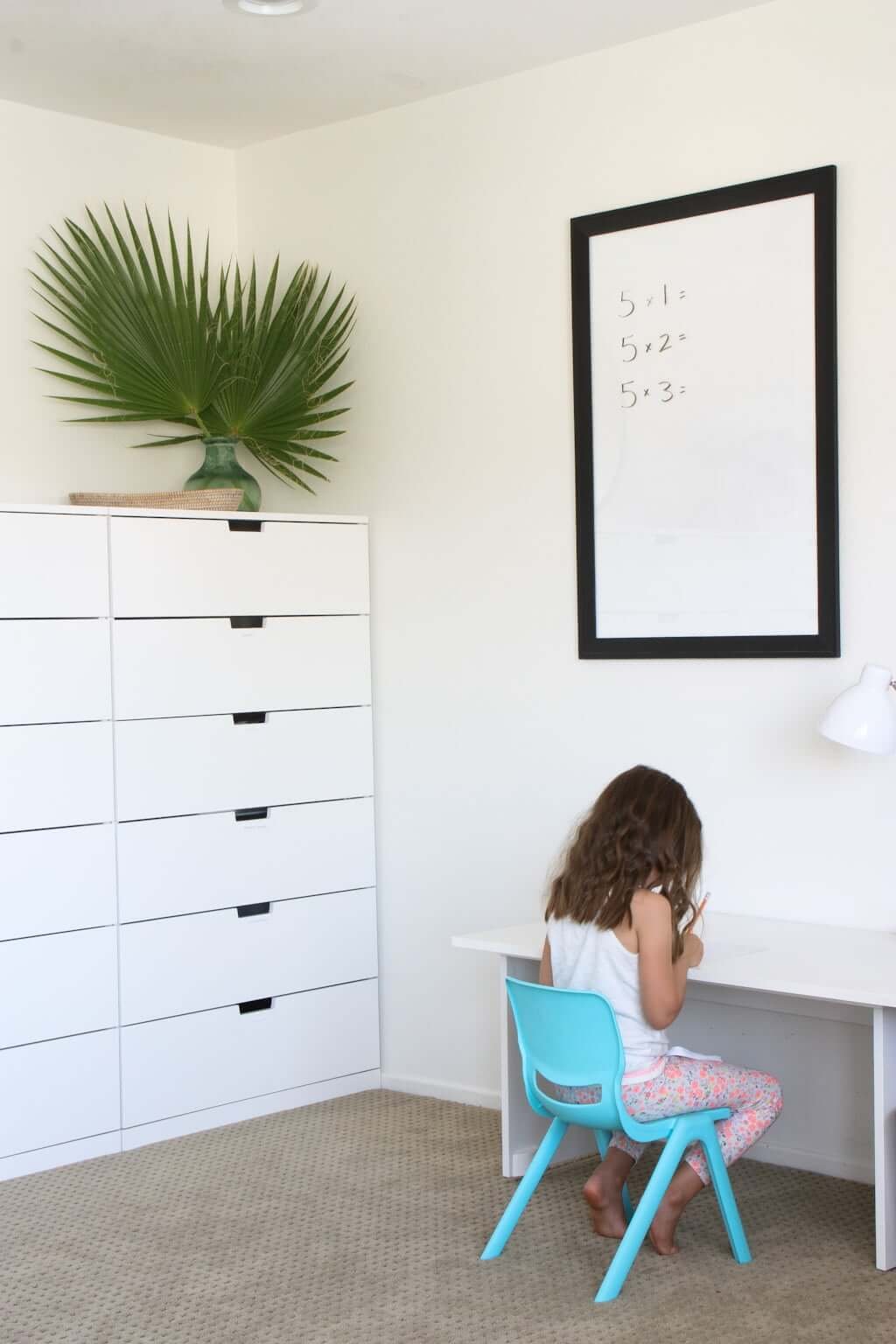 child writing at desk in IKEA homeschool room with white board above and IKEA storage drawers to left