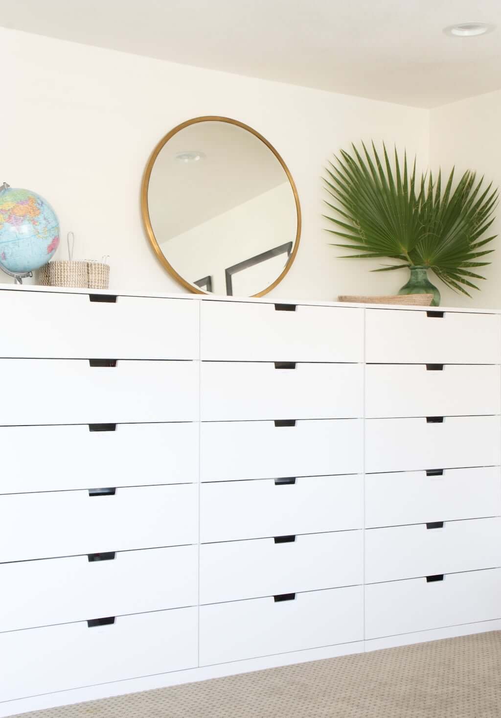 wall of white IKEA homeschool drawer storage with round mirror, globe, and plant