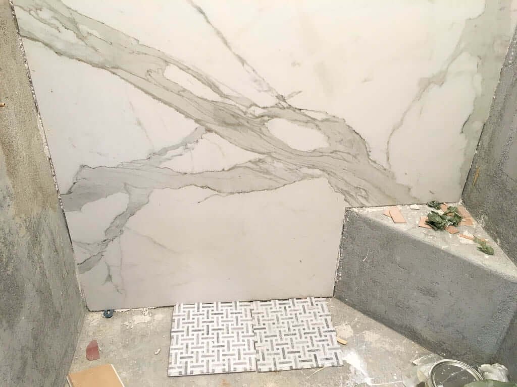 unfinished shower floor with marble floor tiles being tested against shower wall