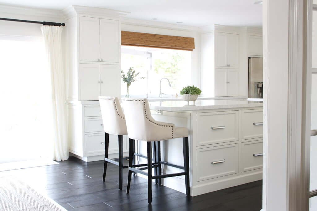 white kitchen with island and barstool chairs, dark wood flooring