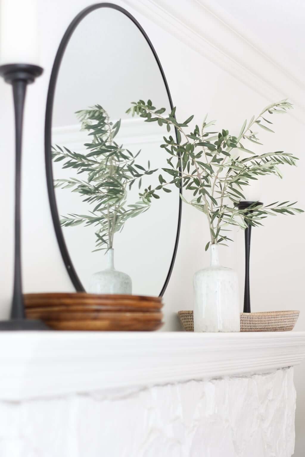 closeup of minimal fireplace mantel with mirror, vase, plates, candlesticks, and basket