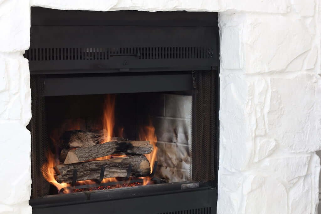 gas fireplace with white painted stone facade and split oak logs in fireplace lit