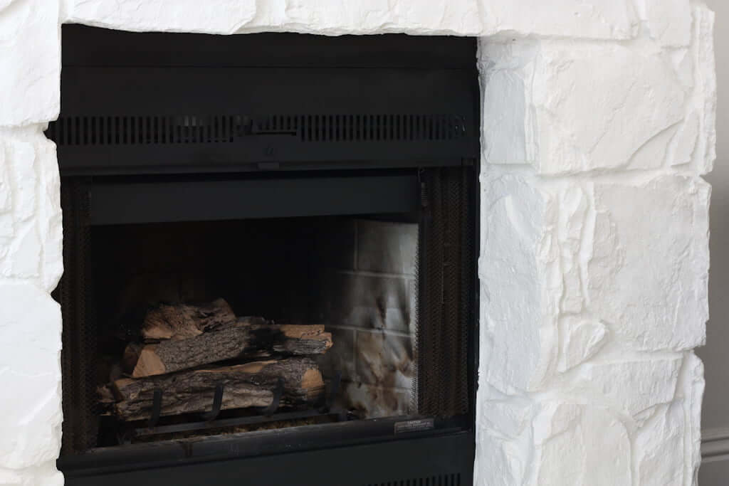 gas fireplace with white painted stone facade and split oak logs in fireplace