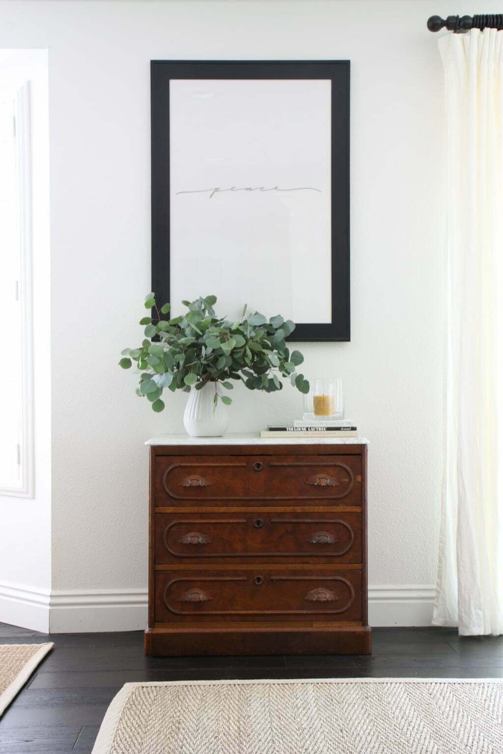 frame on wall with antique bureau below, eucalyptus in vase with candle