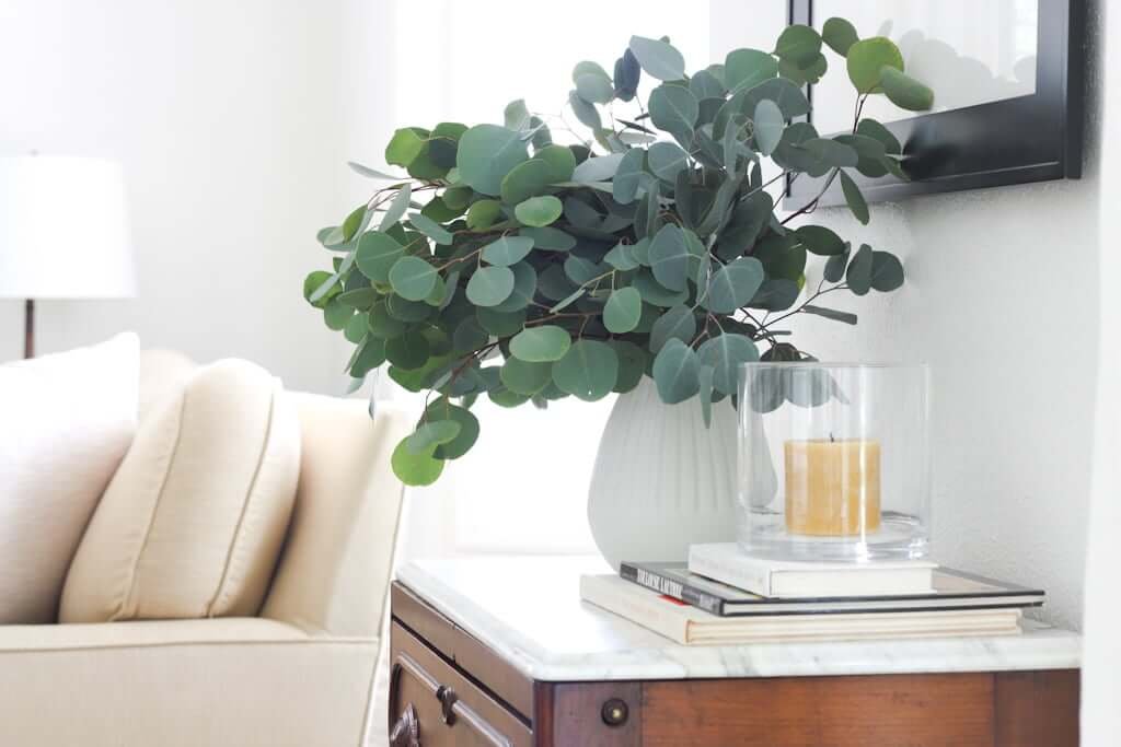 console styled with eucalyptus in vase, candle, couch in background