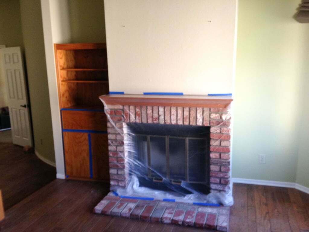 brick fireplace prepped to be painted, with plastic and painters tape over it