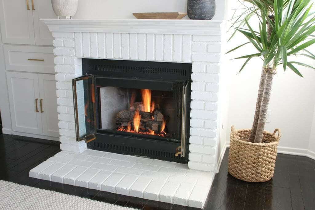 painted brick fireplace after, white brick with fire and plant to side