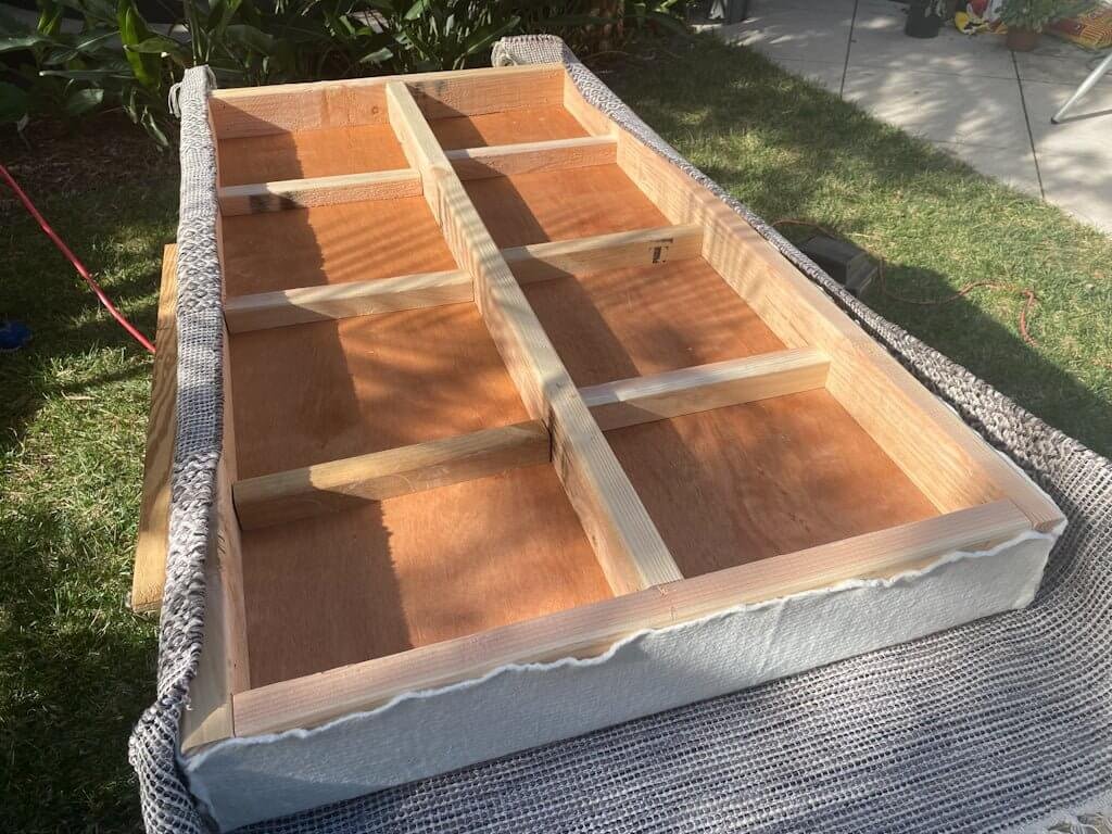 Wooden underside of easy diy ottoman showing batting and rug