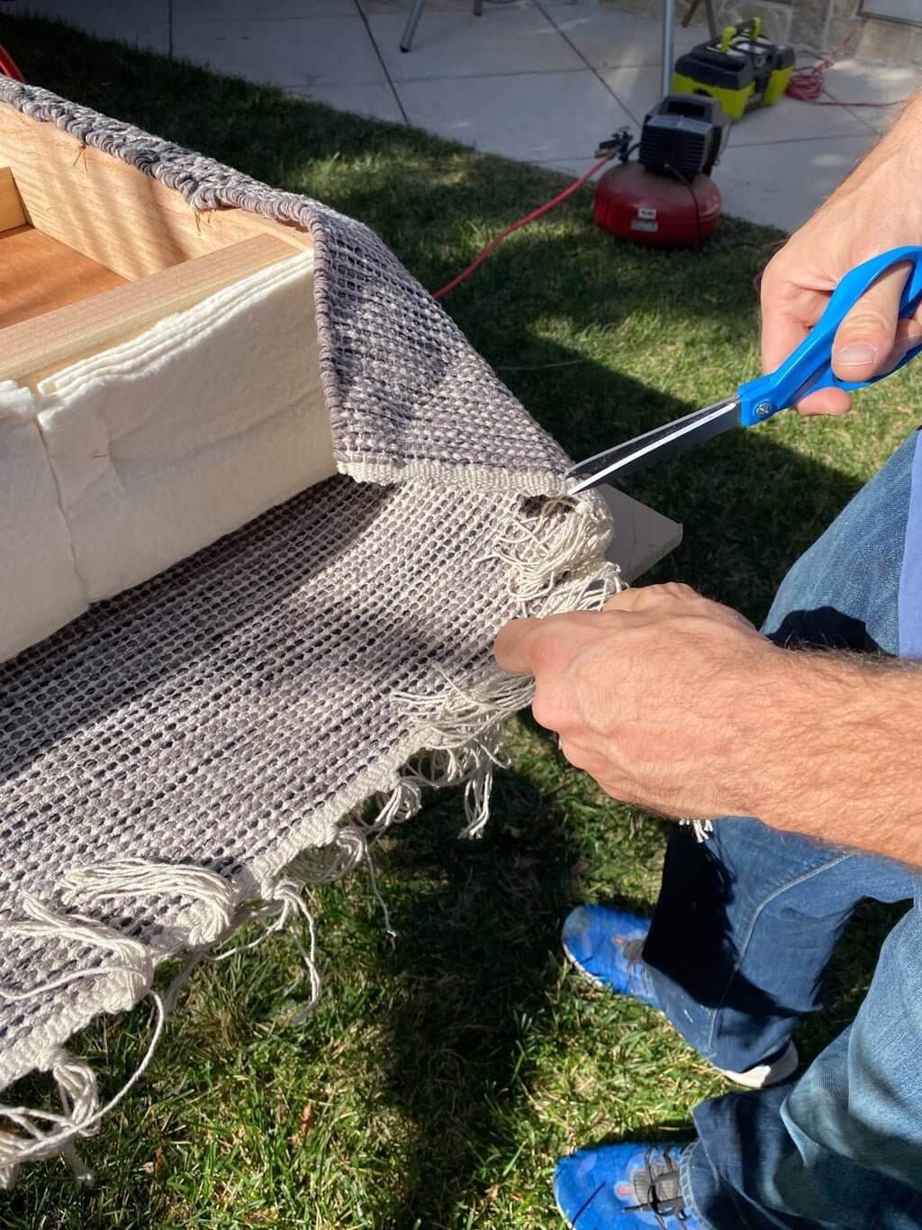 man cutting tassles from rug covered ottoman