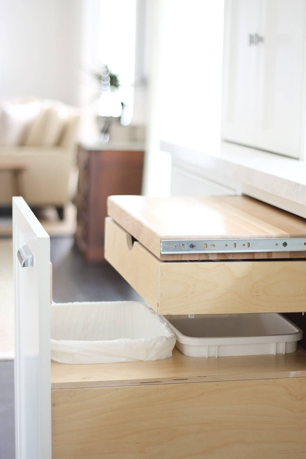 kitchen organization idea with pull out cutting board made of wood above trash can