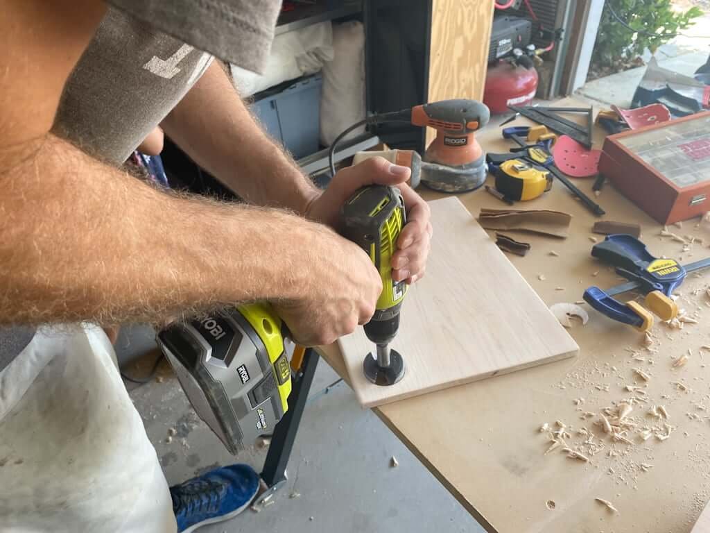 man drilling hole in wooden cutting board with drill bit