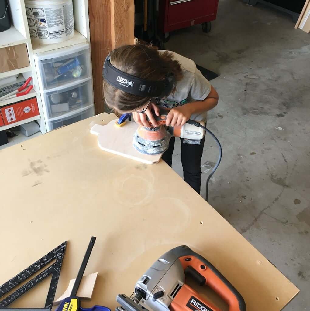 girl sanding wood cutting board with power sander