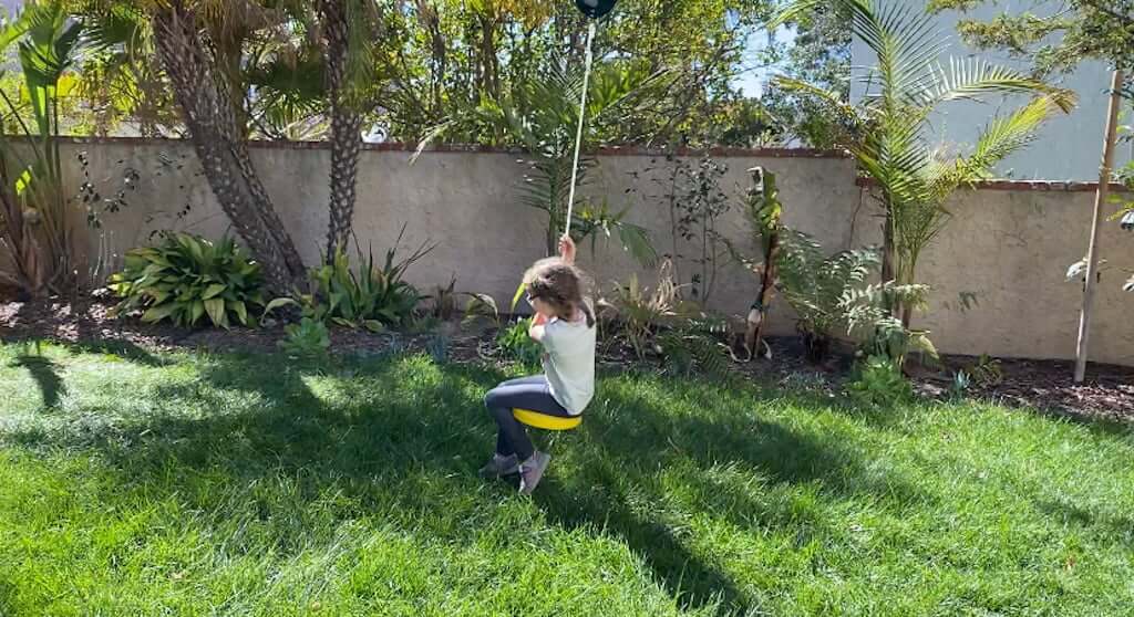 child riding on backyard zipline over lawn 