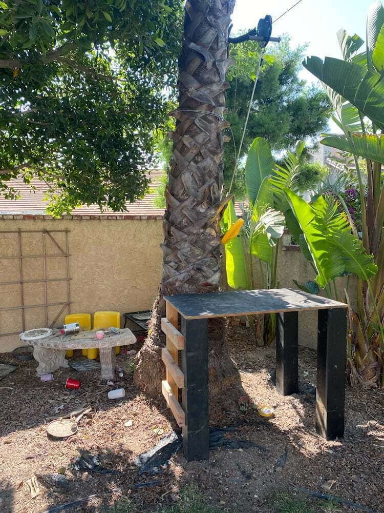 backyard zipline platform next to tree with kids play area on other side