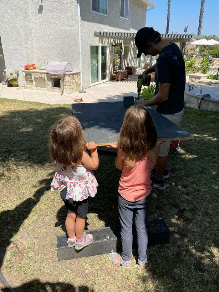 man building a zipline platform in backyard with two children helping hold up