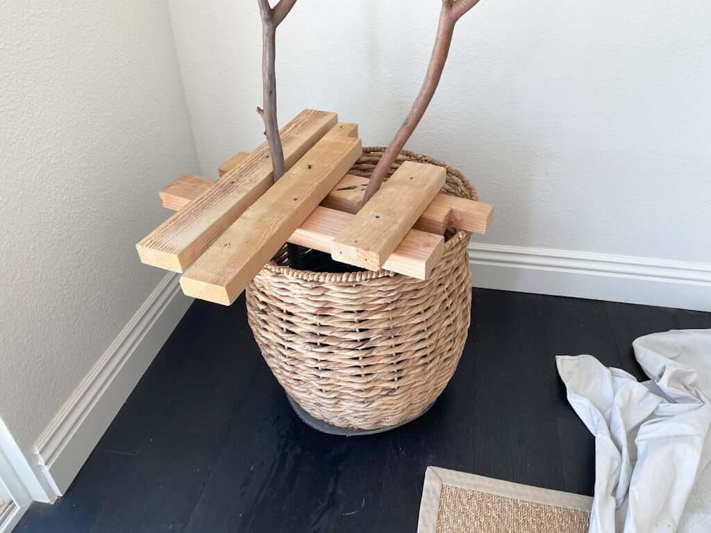 wood holding up fake tree branches in basket