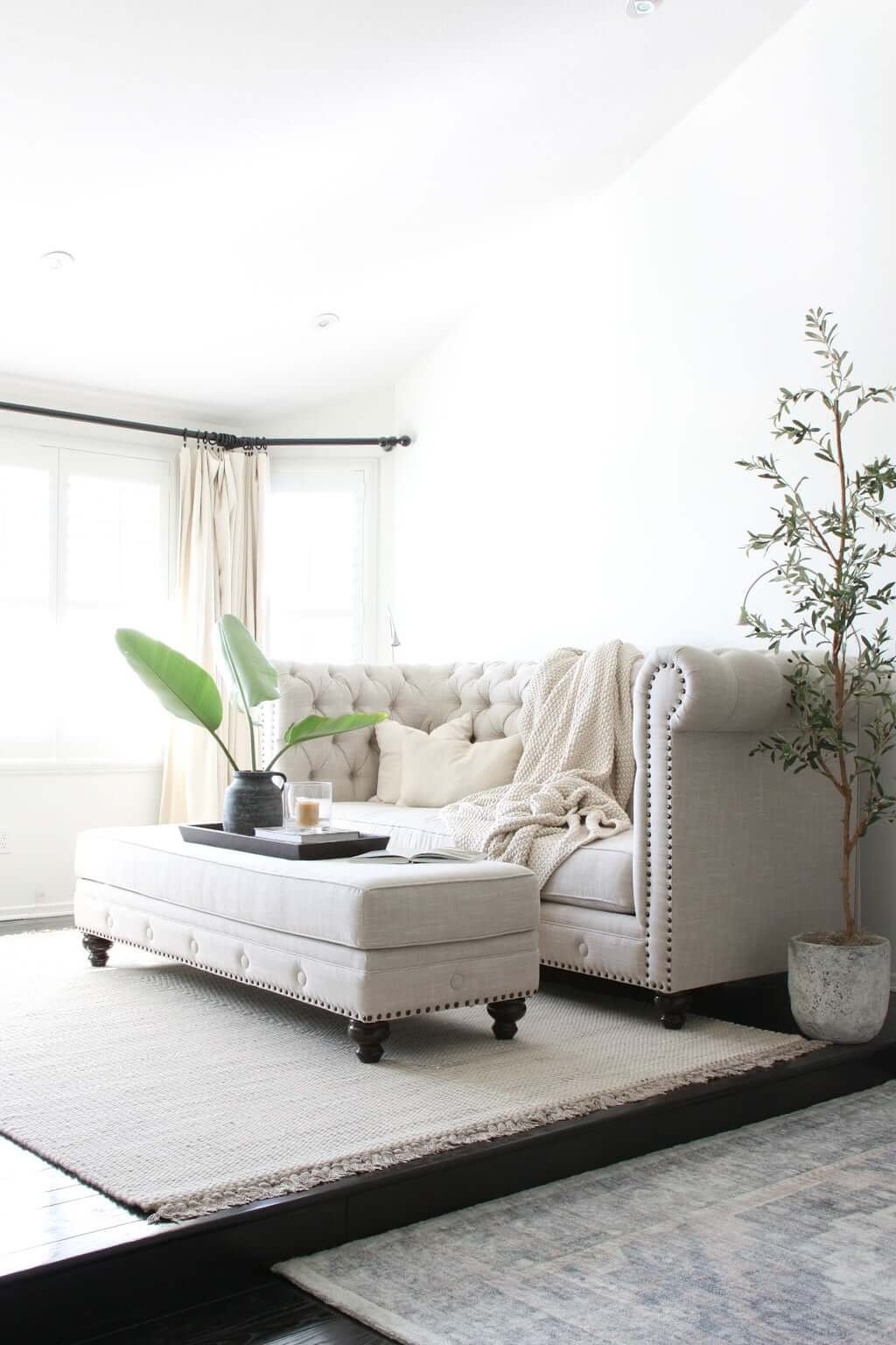 hotel-style seating area in bedroom, with couch and ottoman with light-blocking drapes and rugs on floor