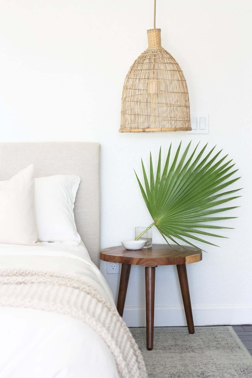 green fan palm in vase on wooden bedside table, bedroom looks like a hotel