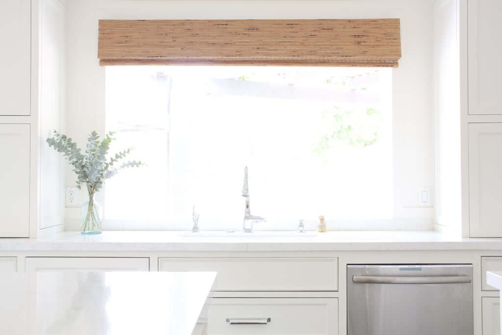 white quartz countertops around kitchen sink with window above and cordless bamboo shade above window