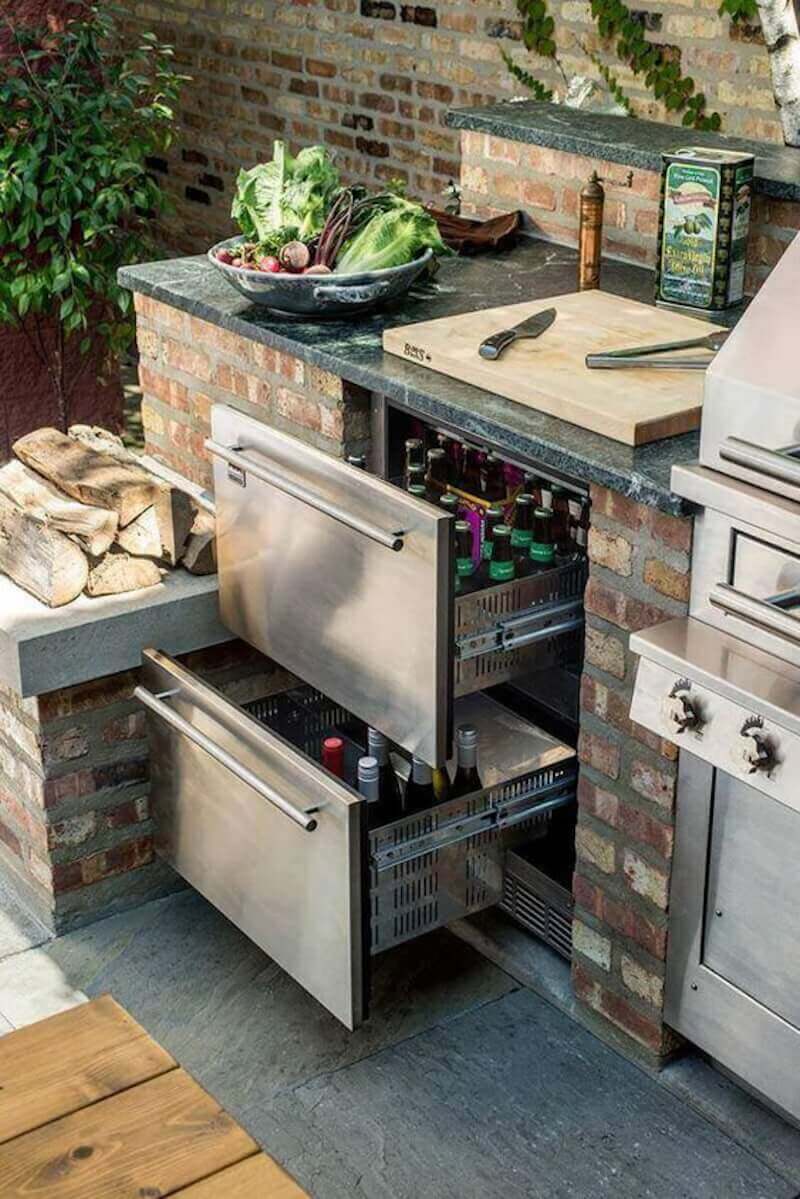 two outdoor stainless steel drawers for beverages and refrigerator next to outdoor grill in backyard kitchen