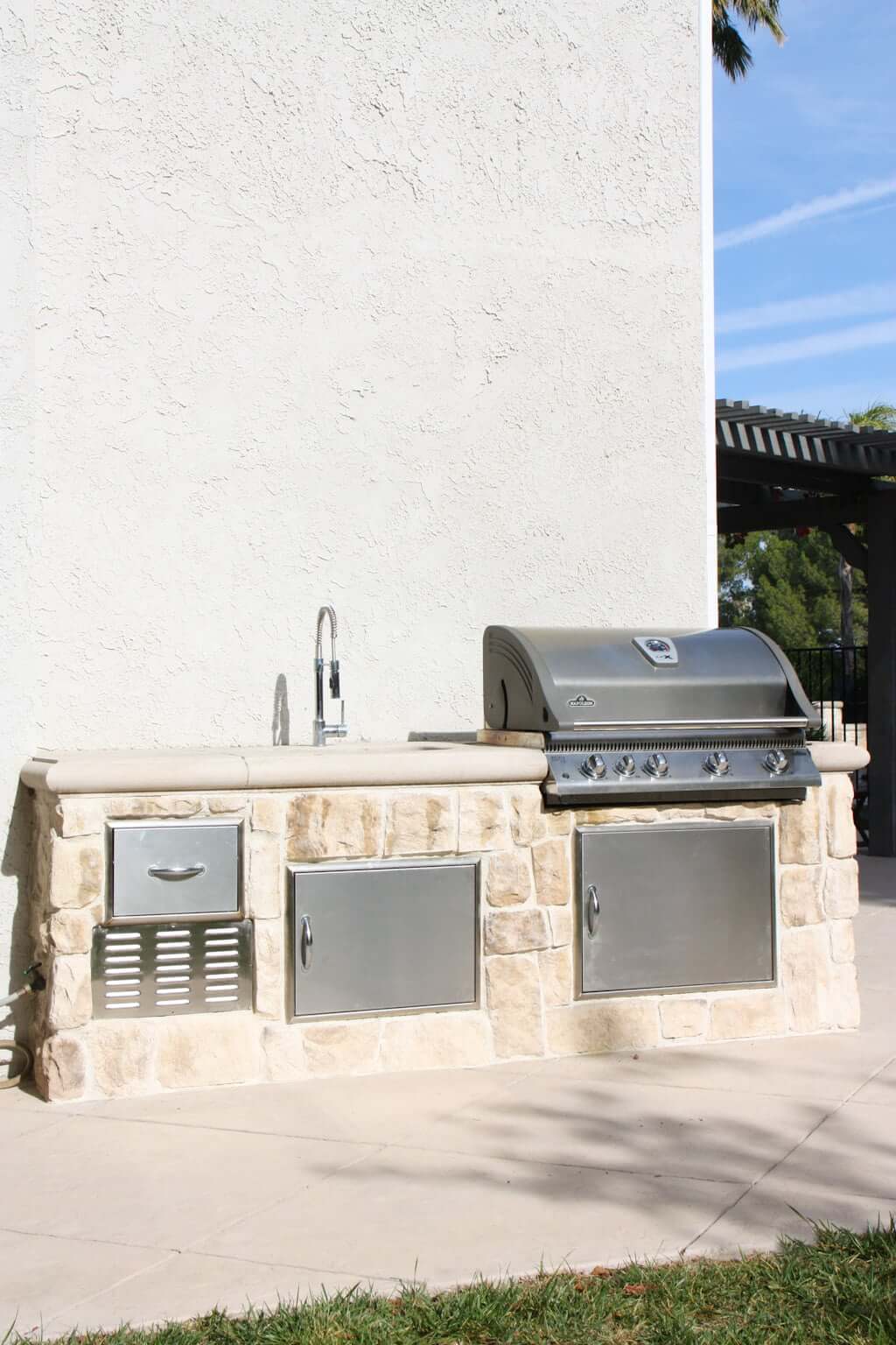 outdoor kitchen sink with stainless steel BBQ and cabinets and stone veneer alongside house