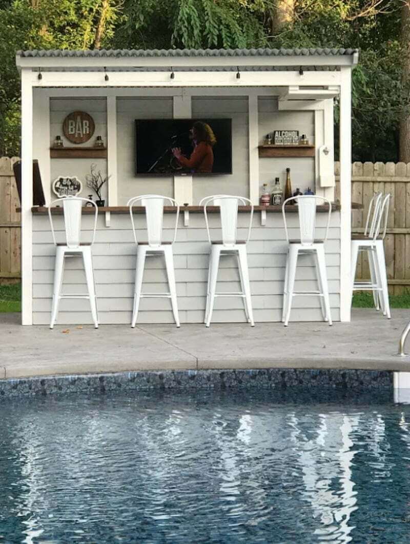 white backyard bar shed with white metal outdoor barstools next to a pool