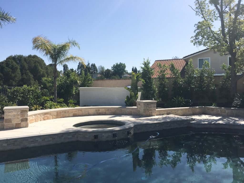 view across pool and jacuzzi to DIY outdoor bar with stucco wall and temporary white counter top next to palm tree and other landscaping