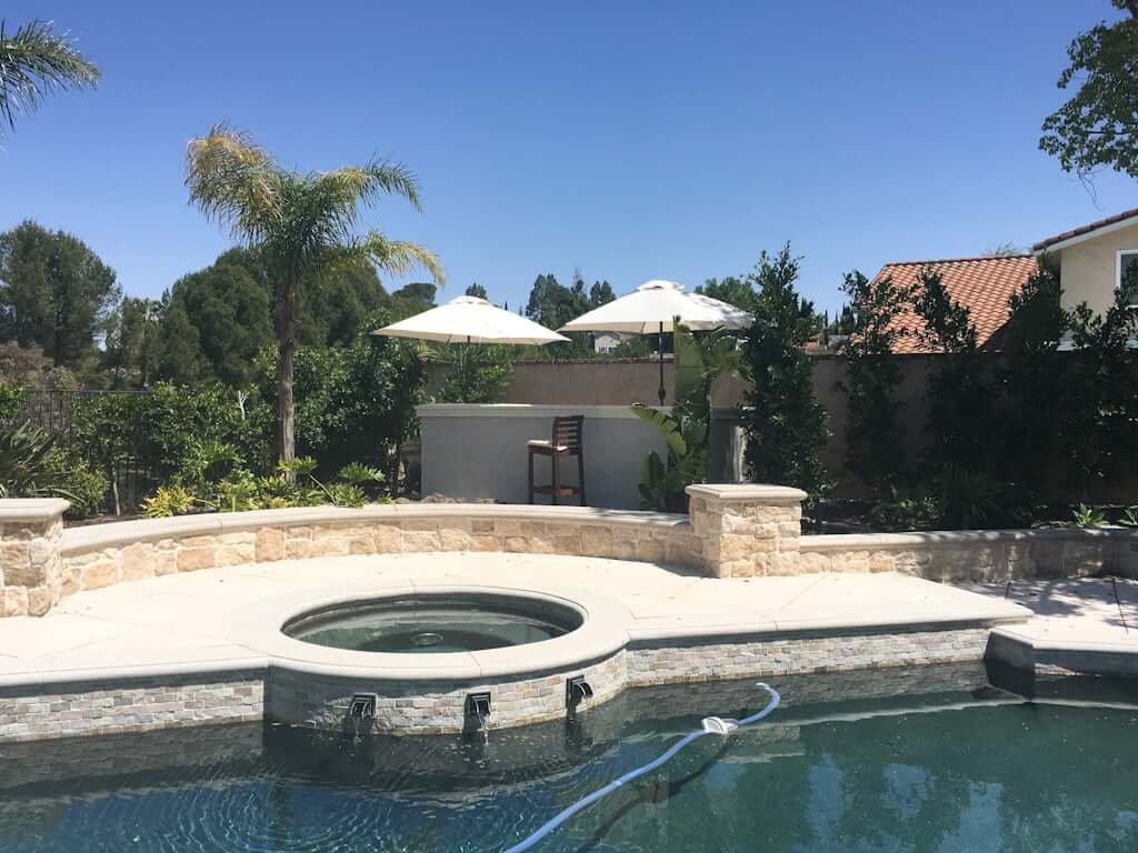 view across pool to DIY outdoor bar with umbrellas and outdoor barstools, with landscaping around it