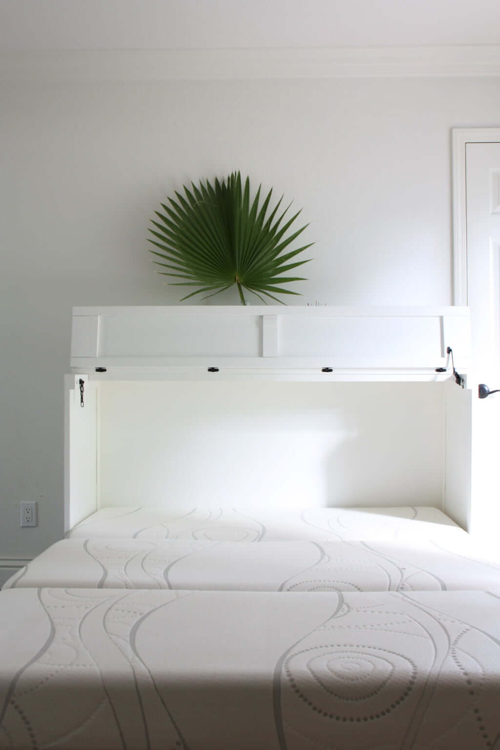 white murphy bed cabinet queen in guest room with white walls and fan palm being folded out