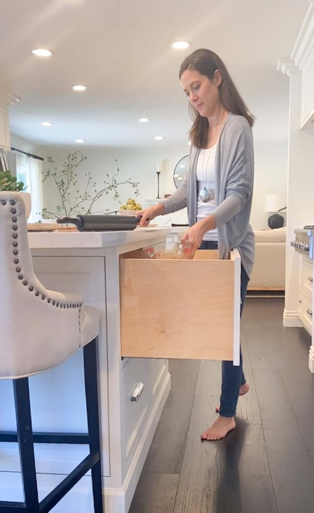 women pulling rolling pin and measuring cups out of kitchen baking drawer in island