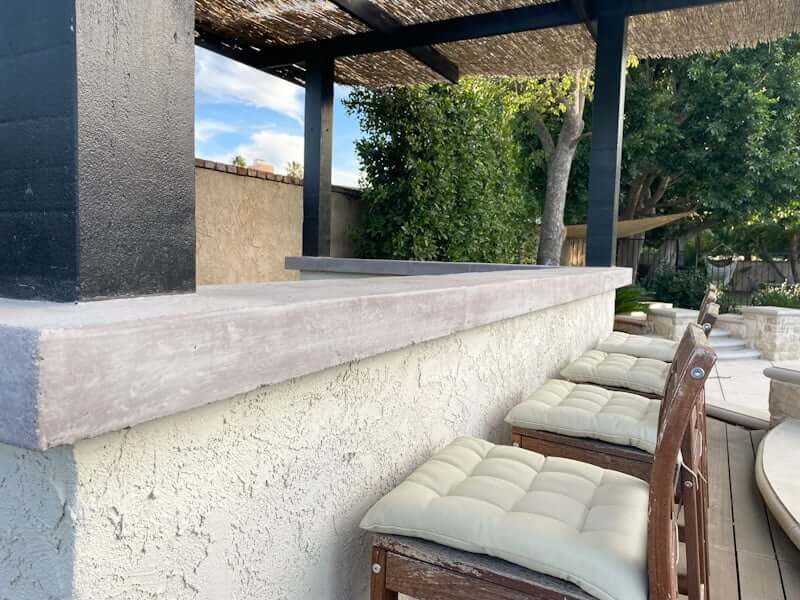 DIY outdoor countertops made of concrete with stucco wall and bar stools and pergola with thatch roof