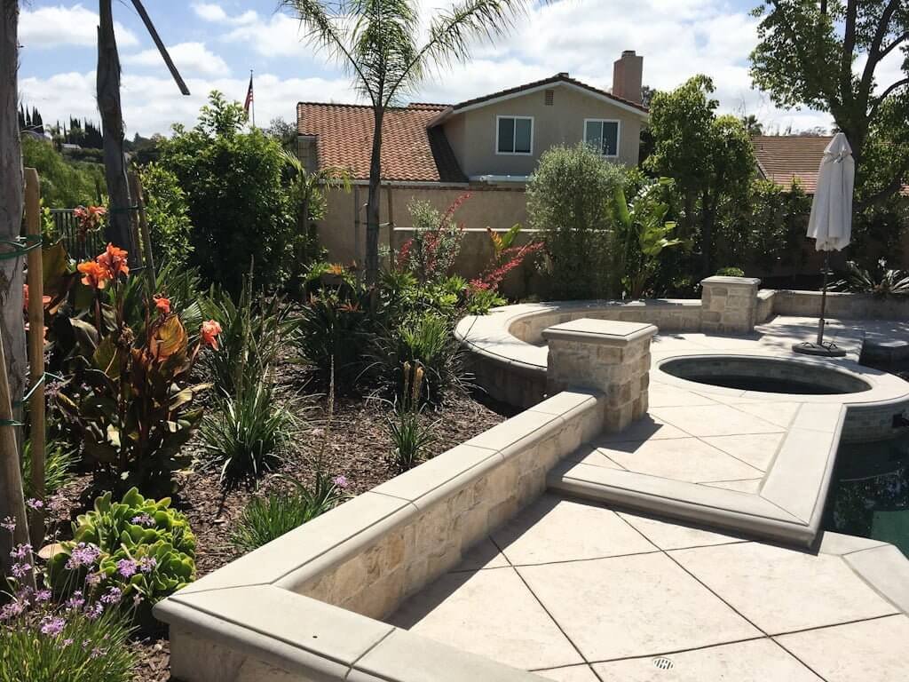 concrete patio and retaining walls around pool with landscaping to hide pool equipment