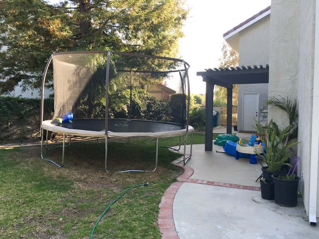 trampoline with net above ground in side yard of house with kids toys