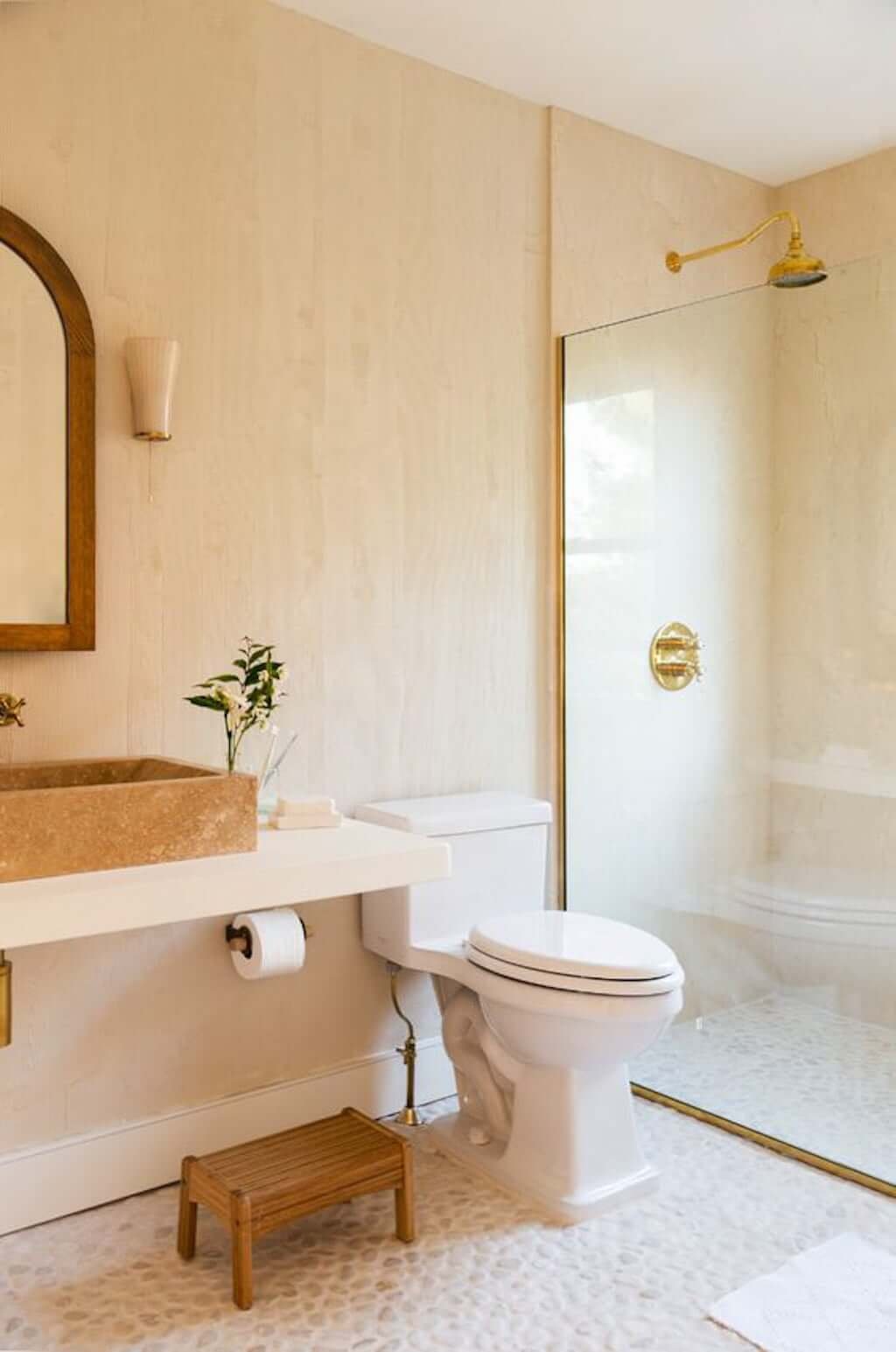 warm colored bathroom with wood walls and stone pebble floor with toilet and stone sink