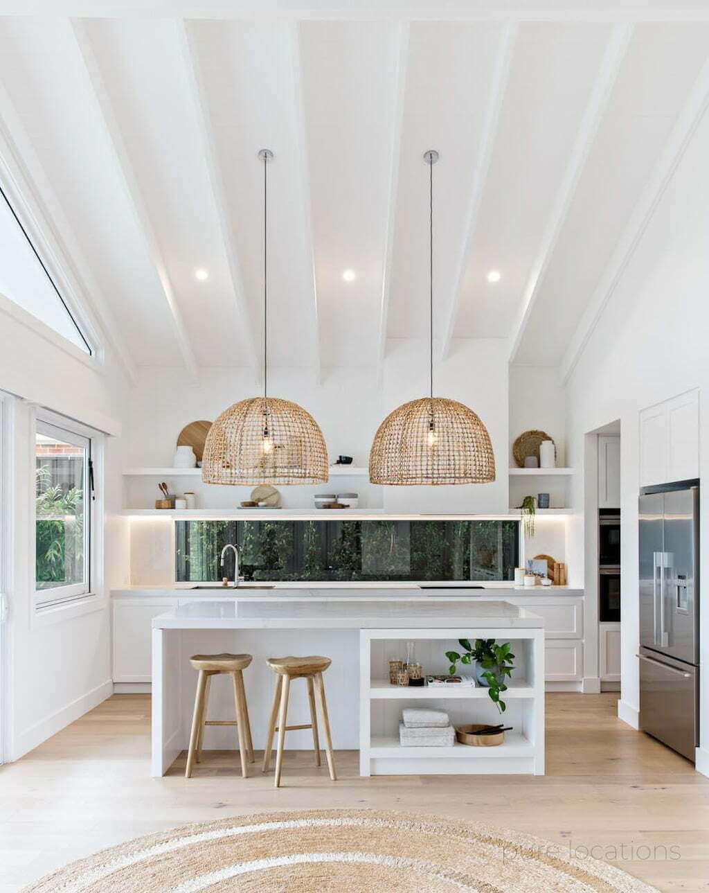 white kitchen with woven pendants, island, and wood floors with window above countertop looking outside