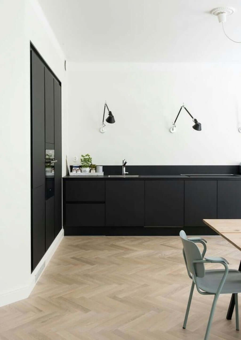 white kitchen with black cabinets, black sconces, and wood herringbone floors