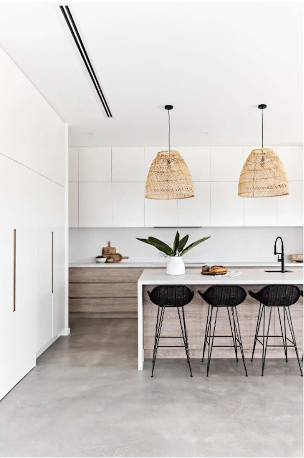 modern beach house kitchen with concrete floors, woven pendants, black barstools, and wood and white cabinets